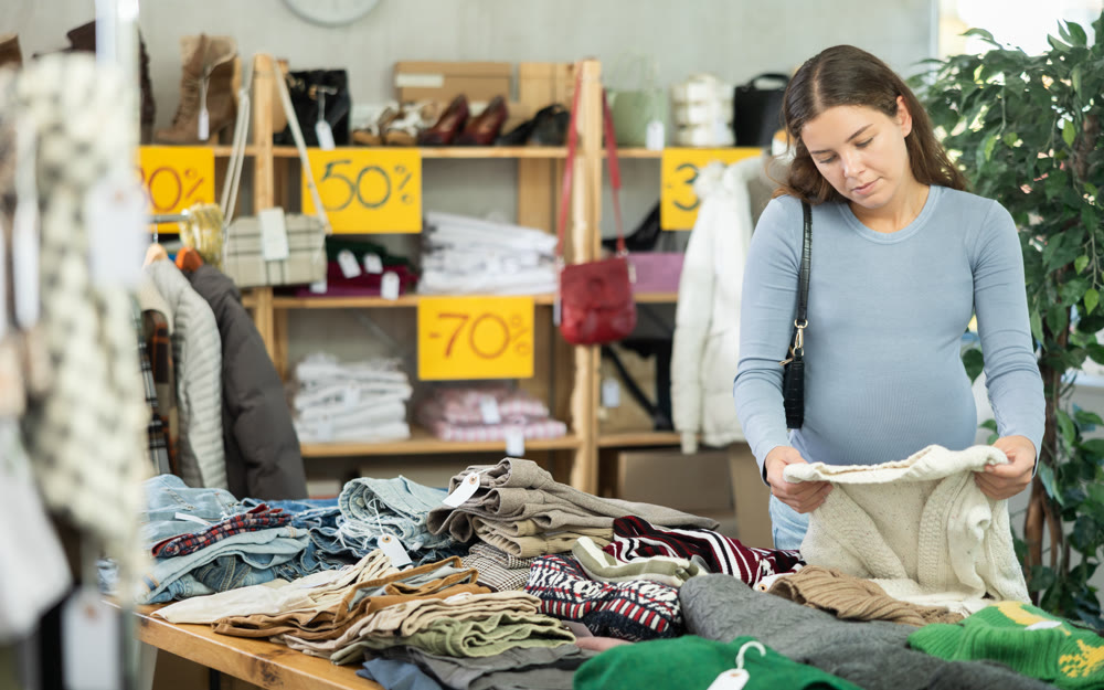 Pregnant woman chooses warm winter sweater in clothing store