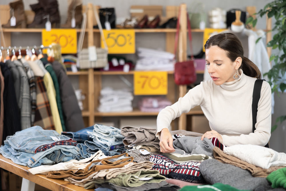 Happy woman chooses fashionable sweater for autumn winter season in store