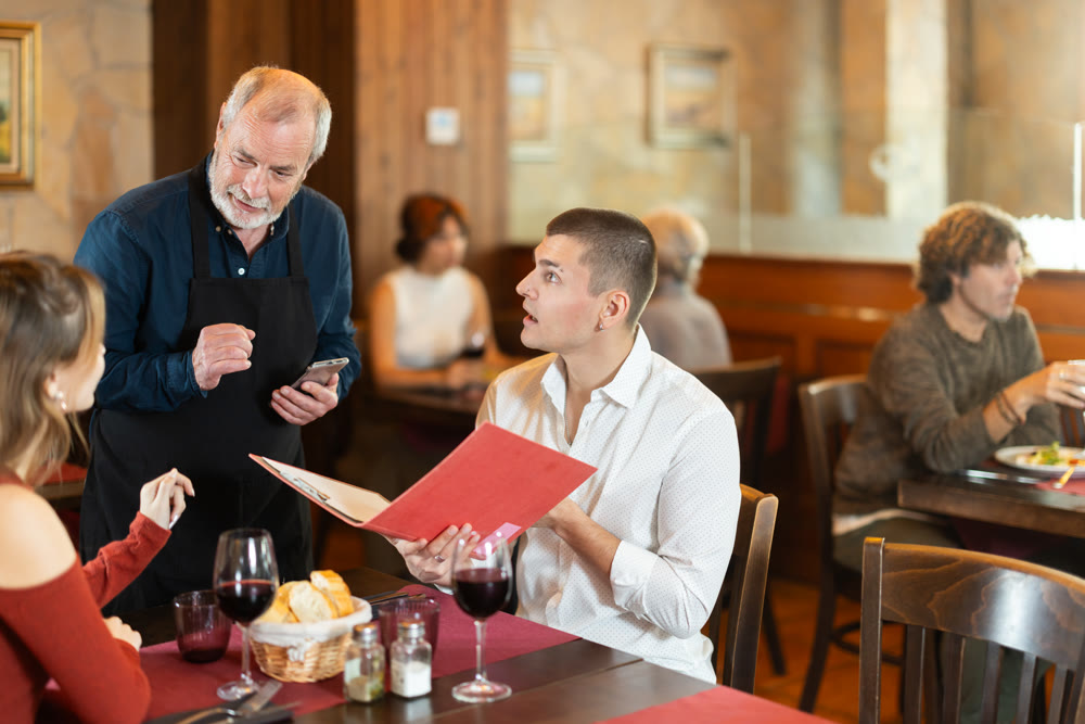 Elderly male waiter takes order from young couple