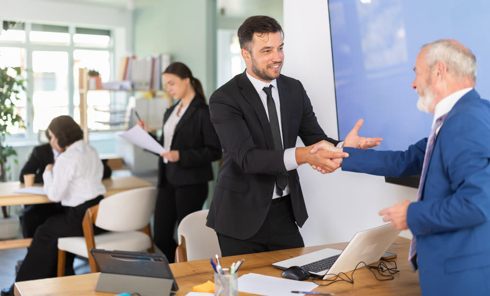 Adult bank manager shaking hands with elderly male client
