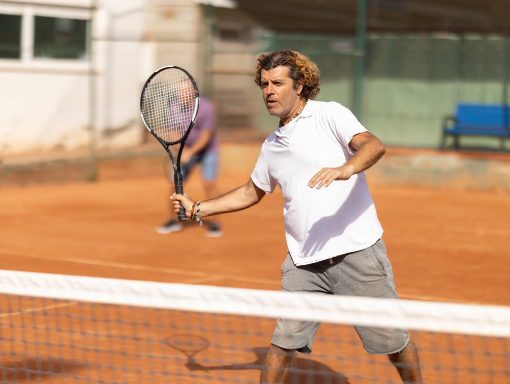Handsome athletic man serving with racket in hands while practicing on tennis court in day