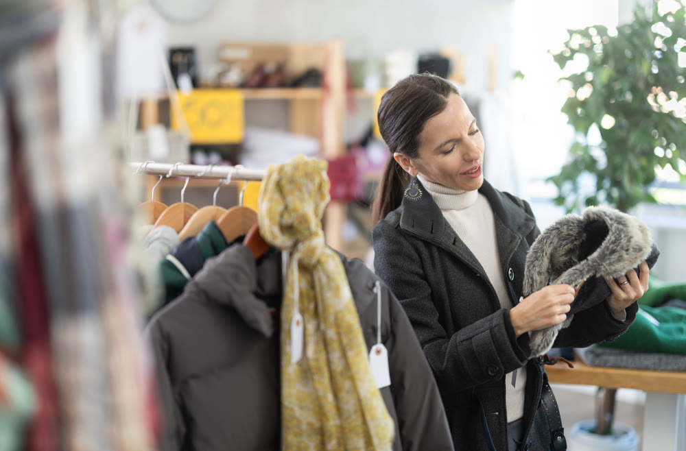 Glad middle-aged woman choosing fur hat in clothing store