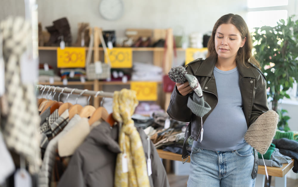 Pregnant woman chooses warm autumn hat in clothing store