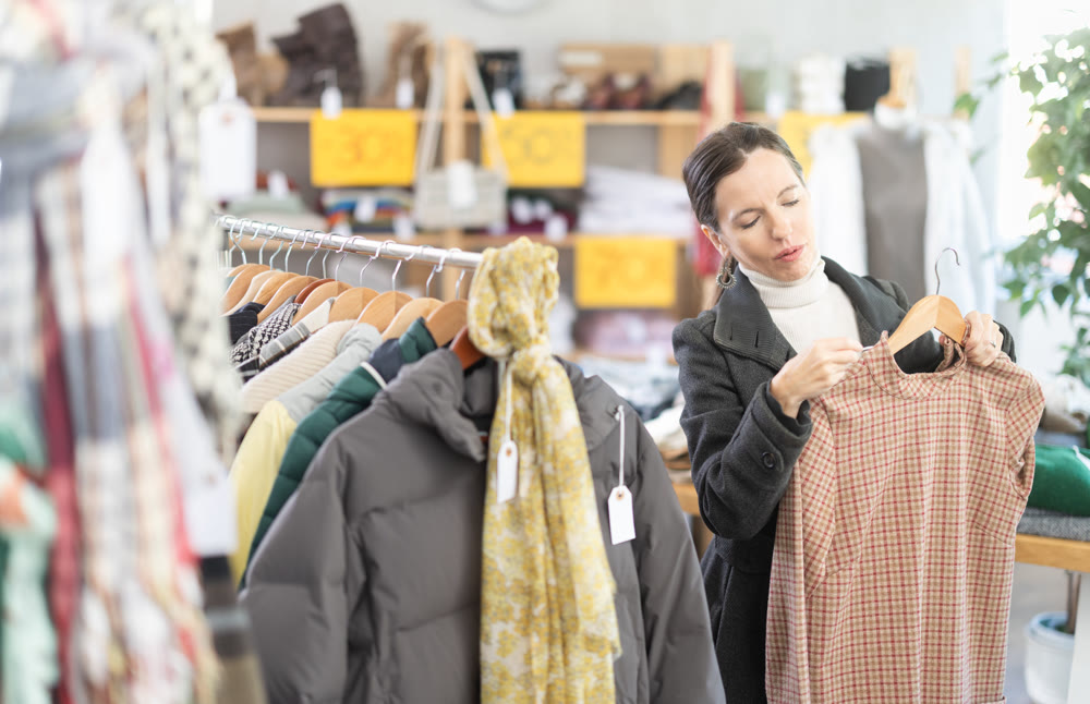 Happy woman chooses fashionable dress for autumn winter season in store