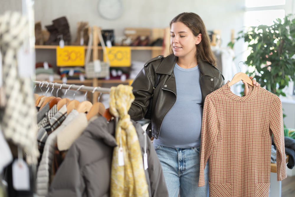 Pregnant woman chooses fashionable dress for autumn-winter season in clothing store