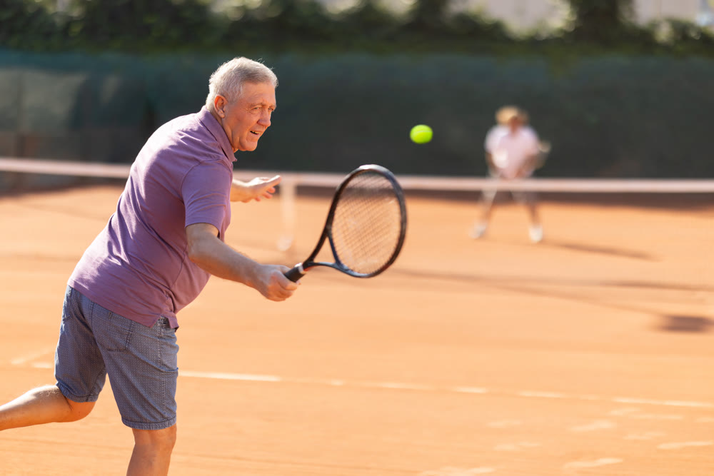 Portrait of european aged male playing paddle tennis with friends on open court in day