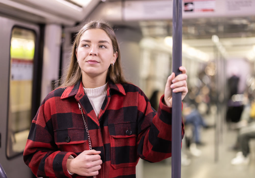 woman stands in a subway car and holds on to a handrail
