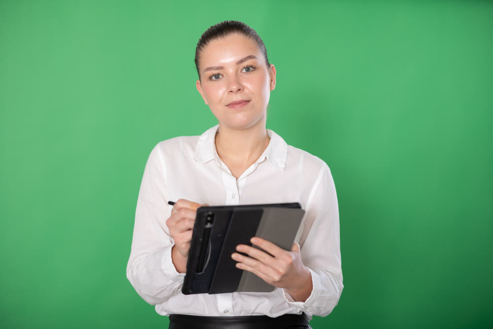 Chroma key compositing. Pretty girl takes notes in electronic tablet on green background