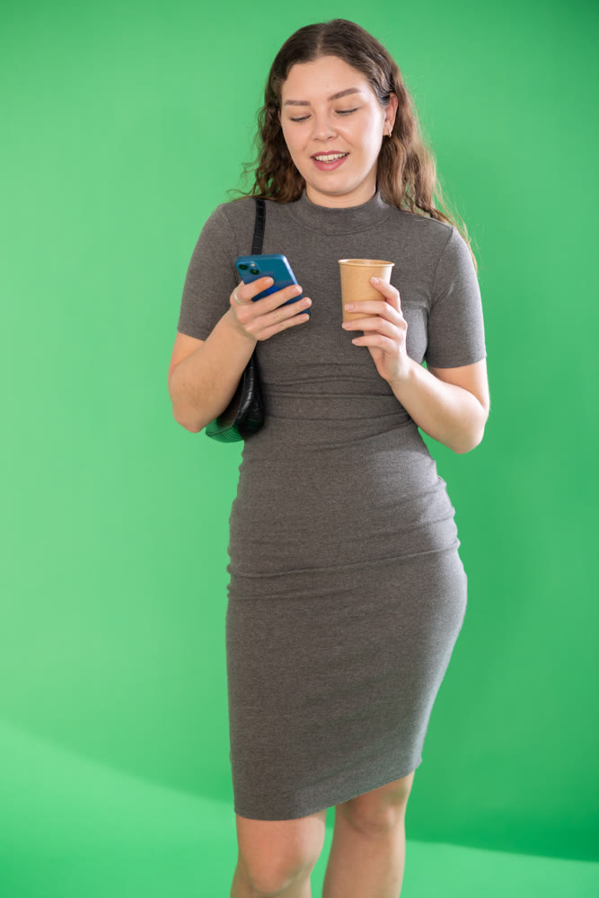 Pretty young woman scrolling through her smartphone screen against and drinking coffee green screen background. Chroma key compositing