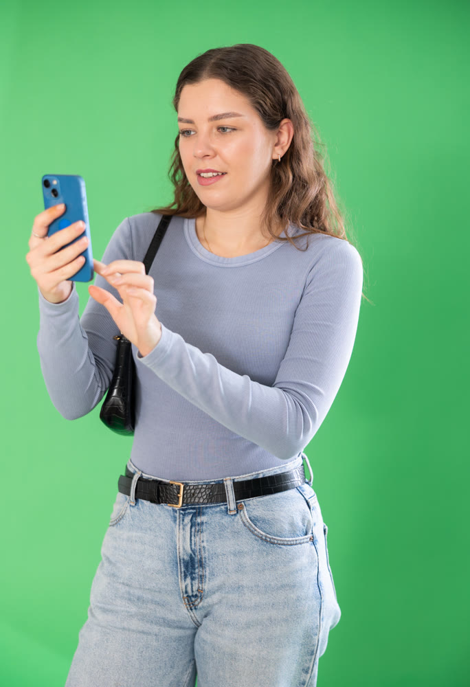 Young woman taking photo or scanning QR code in front of green screen