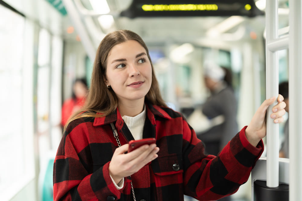 Girl is standing with phone in tram car, getting to work