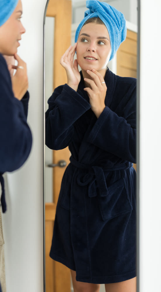 Woman in bathrobe looking in mirror in bedroom interior