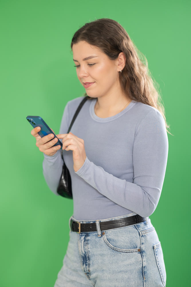 Pretty young girl scrolling through smartphone screen against green screen background. Chroma key compositing.
