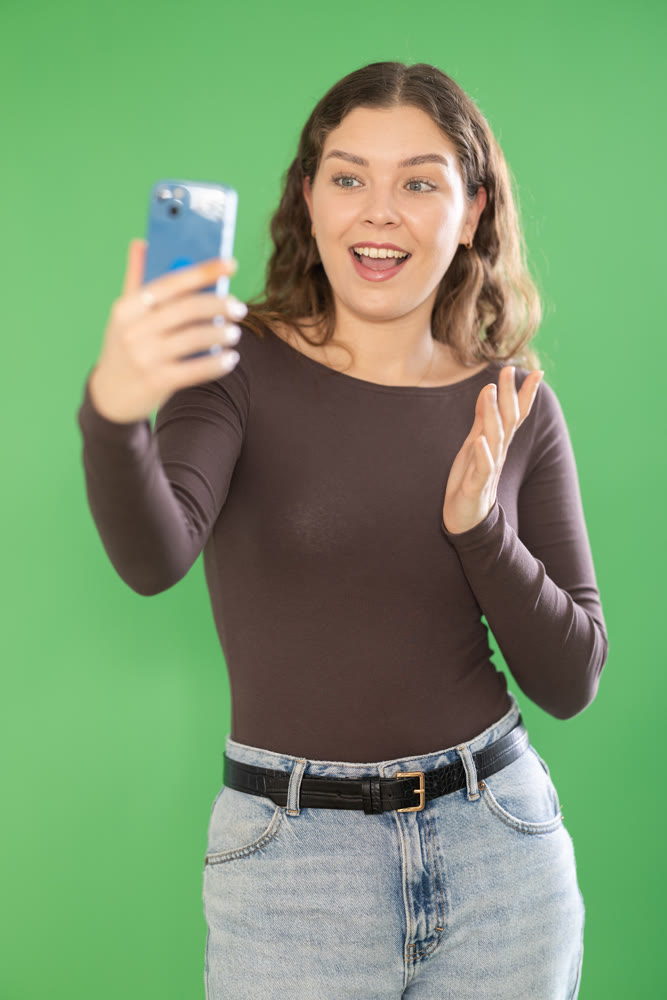 Young woman taking selfie in front of green screen