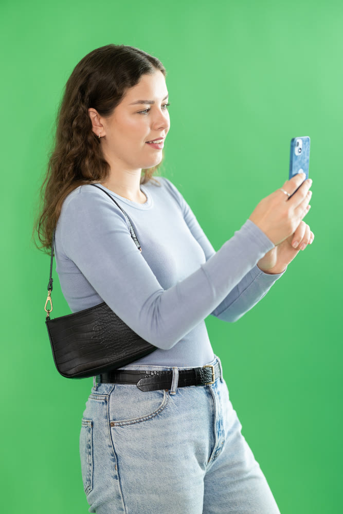 Young woman taking photo or scanning QR code in front of green screen