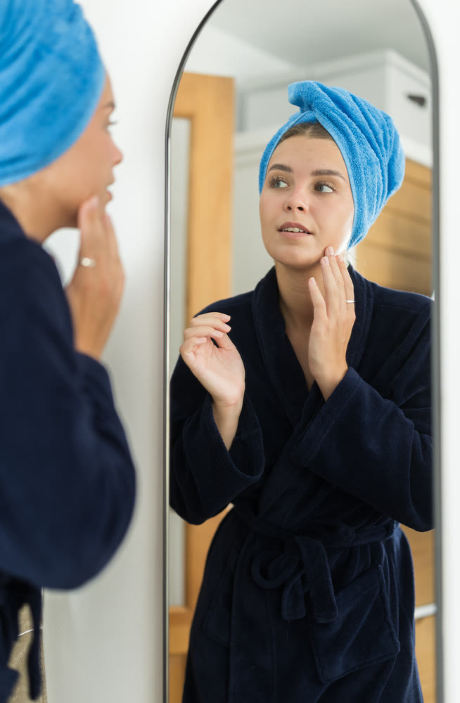 Young woman looking into mirror in bedroom