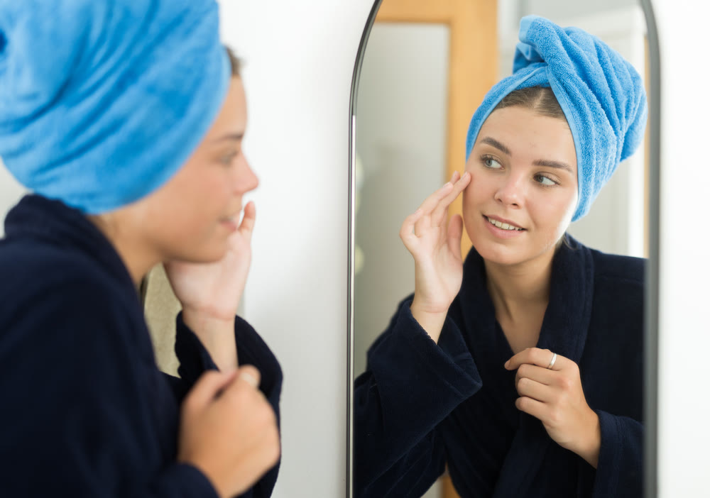 Portrait of attractive young woman wearing in bathrobe standing in front of mirror in cozy bedroom