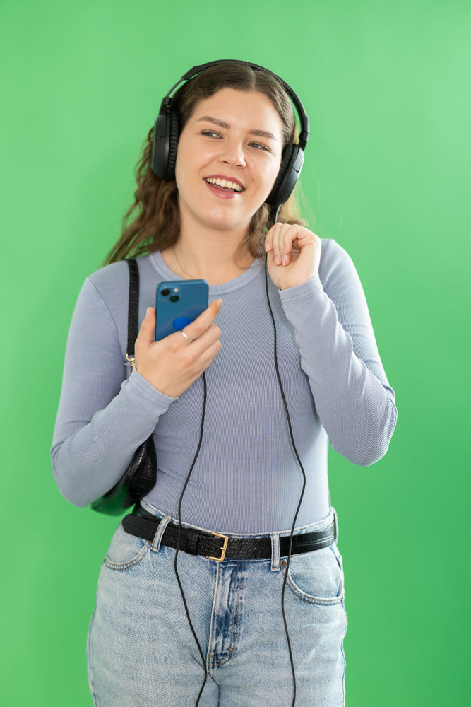Passionate girl listening to music on headphones on green background. Chroma key compositing.