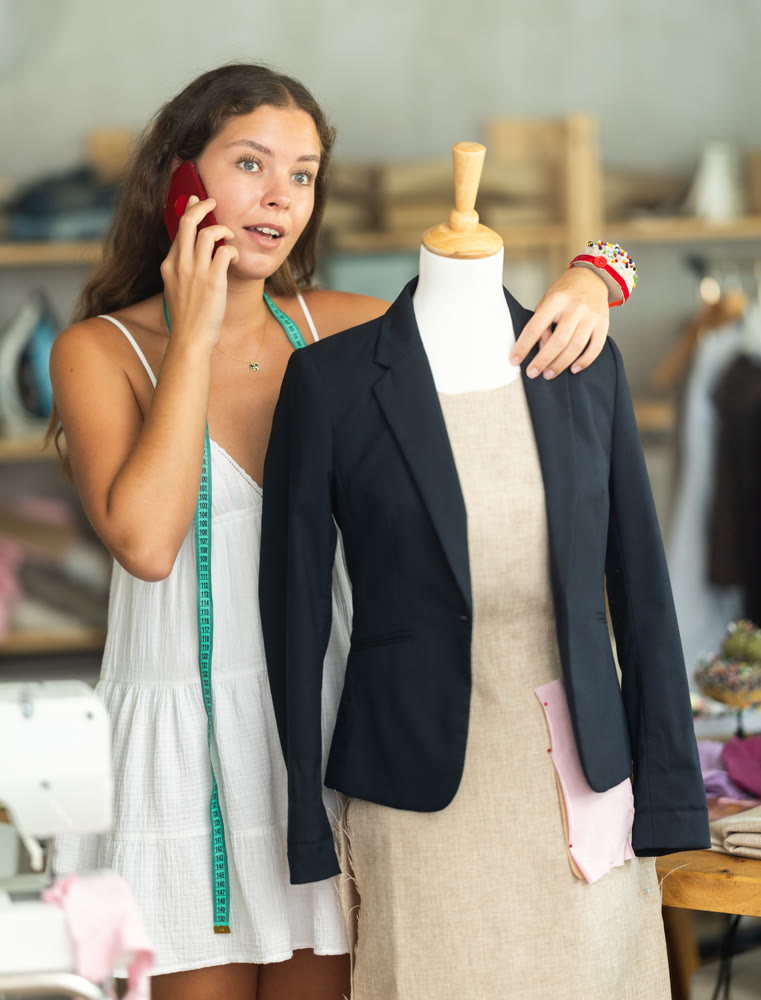 dressmaker stands near the mannequin and talks on her mobile phone