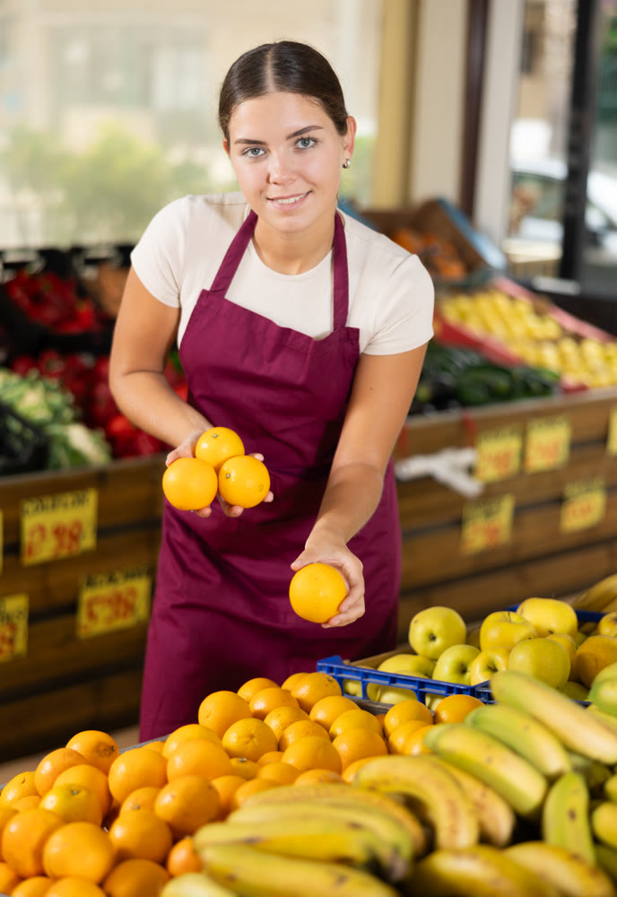 Girl seller working in grocery and lays out fresh oranges on counter
