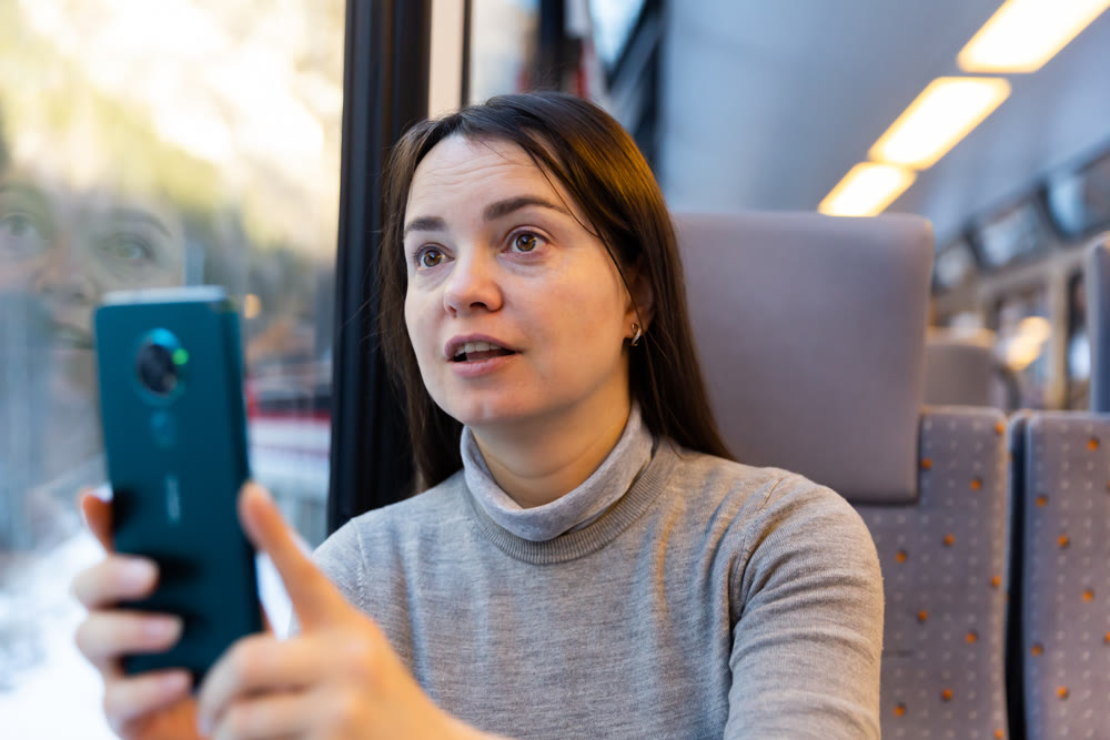 Woman taking photos with smartphone through window glass while travelling by train