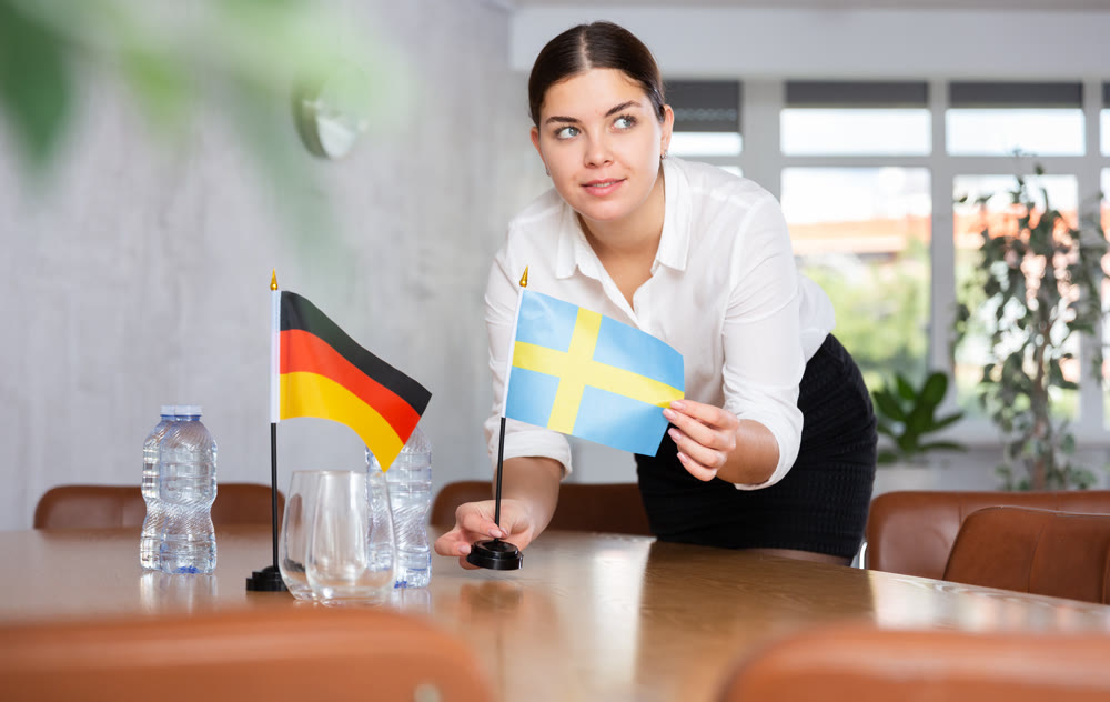 Young female attendant putting up flags for international negotiations between germany and sweden