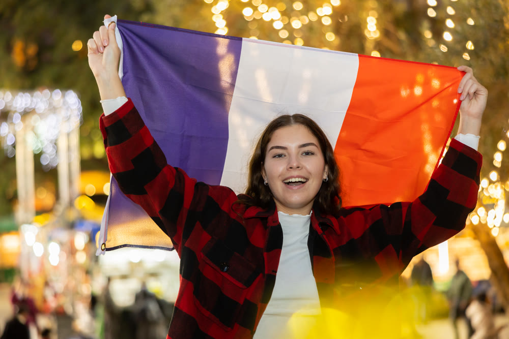 Smiling girl with flag of France walking on street Christmas fair