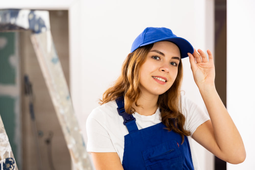 Portrait of contented young female builder in blue overalls during the repair of cottage