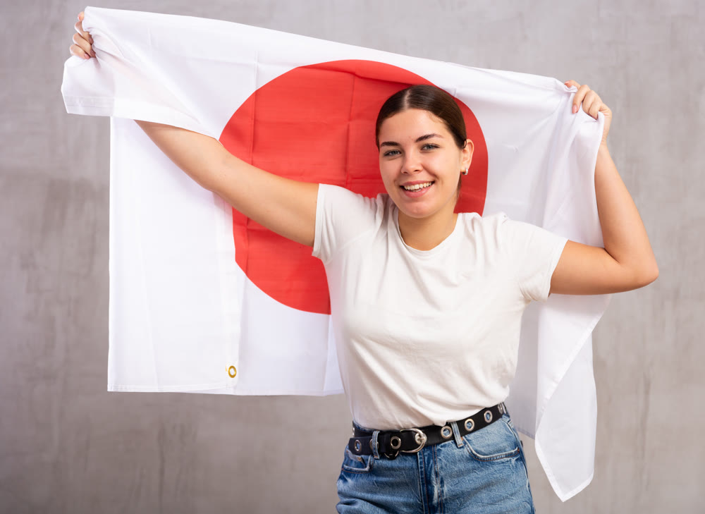 Joyous young woman holding Japan flag against unicoloured background