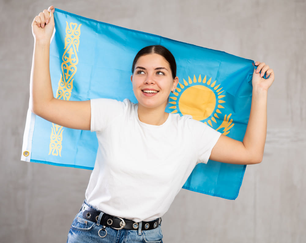 Joyous young woman holding Kazakhstan flag against unicoloured background