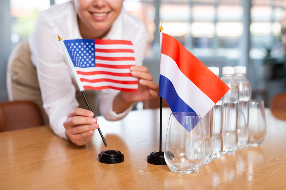 Young woman puts USA and Netherlands flags on table in office