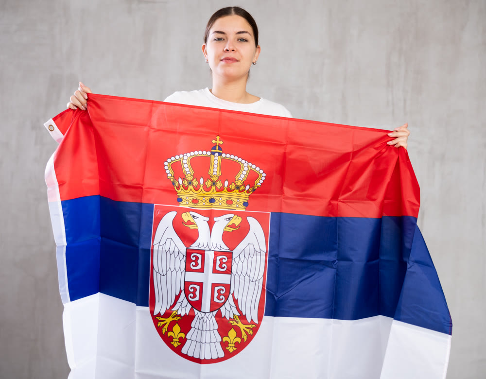 Contented young woman holding Serbia flag against unicoloured background