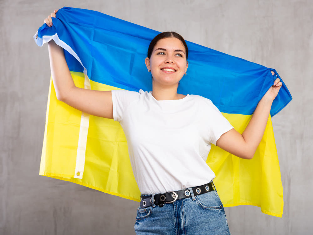 Happy young female student woman with flag of Ukraine against background of gray wall