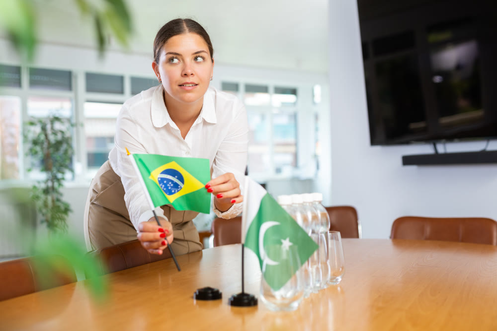 Positive young woman putting little flag of Brazil on table next to the flag of Pakistan