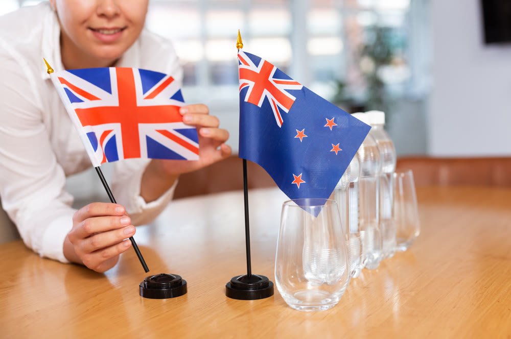 Young woman putting UK and New Zealand flags on table in office