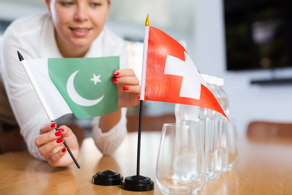 Young woman putting flags of Pakistan and Switzerland on table in office