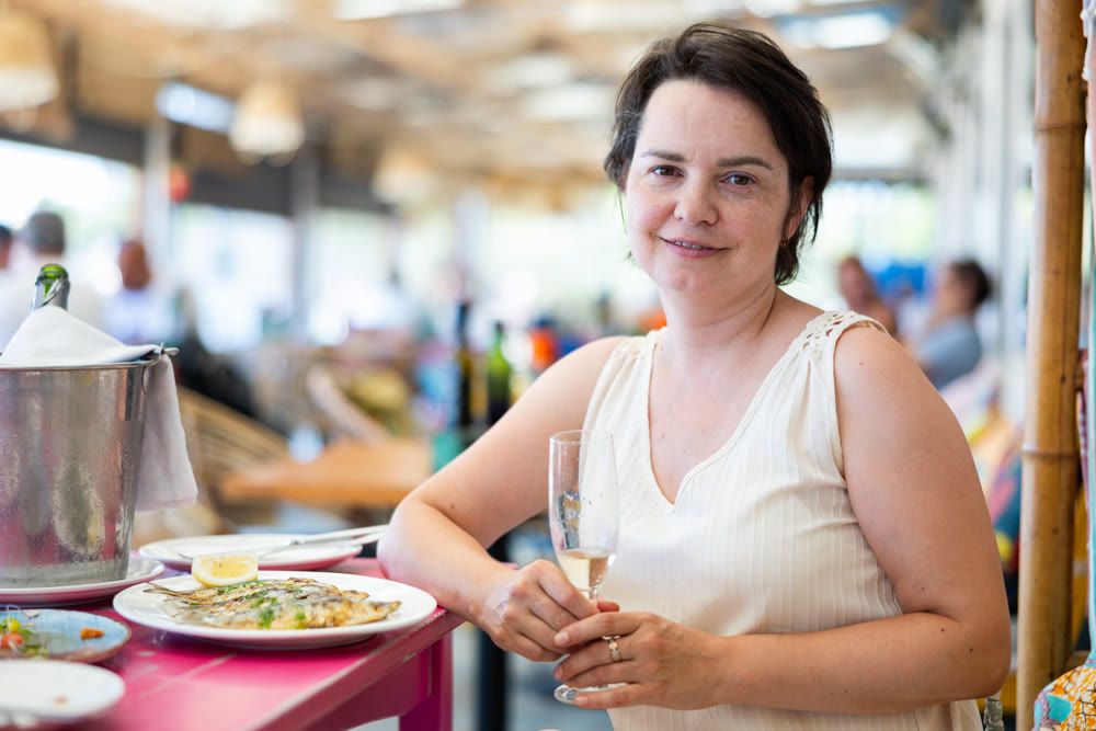 Woman relaxes on terrace of summer cafe and eats grilled sardines