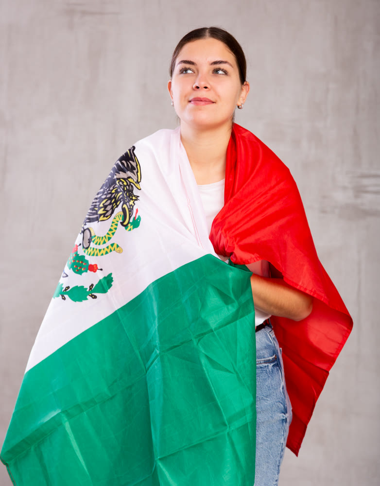 Happy girl stands with flag of Mexico. Isolated on gray background