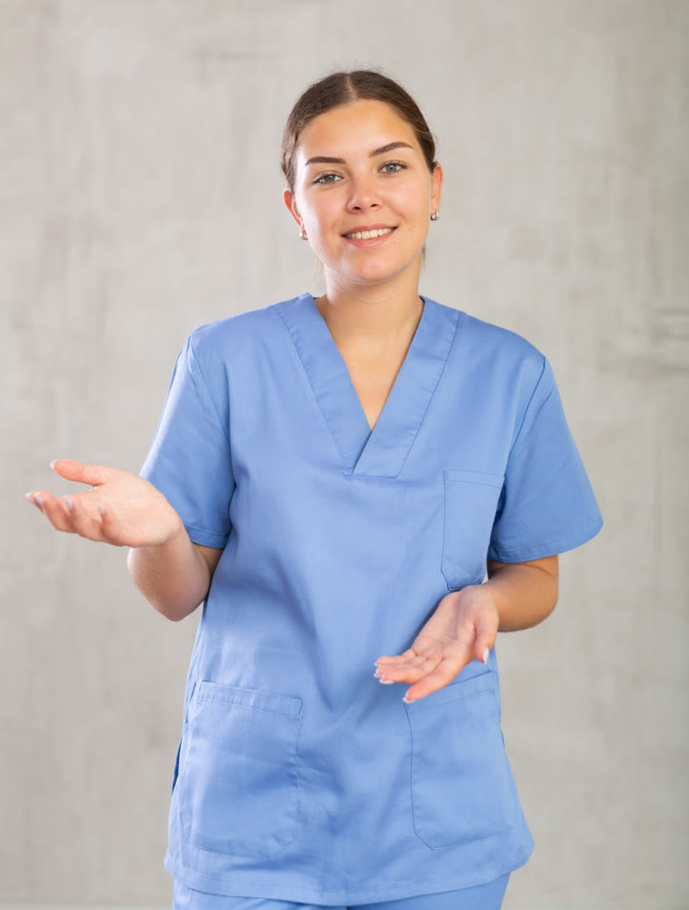 Friendly nurse in blue coat posing against gray studio background, looking at camera with smile