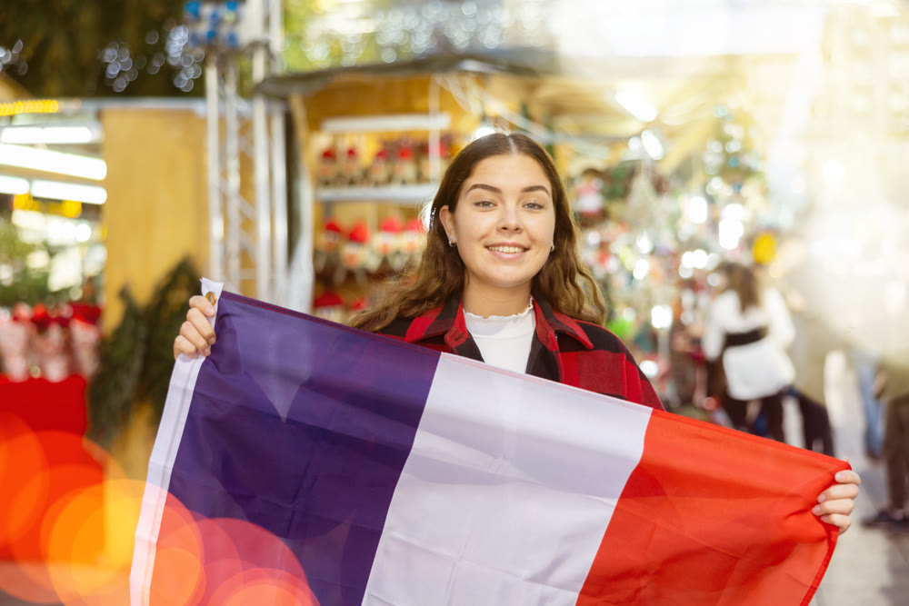 Smiling girl with flag of France walking on street Christmas fair