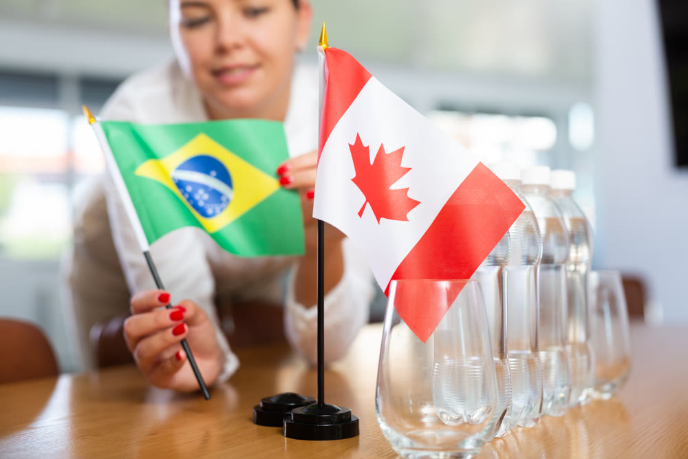 Young woman puts flags of Brazil and Canada on table in office