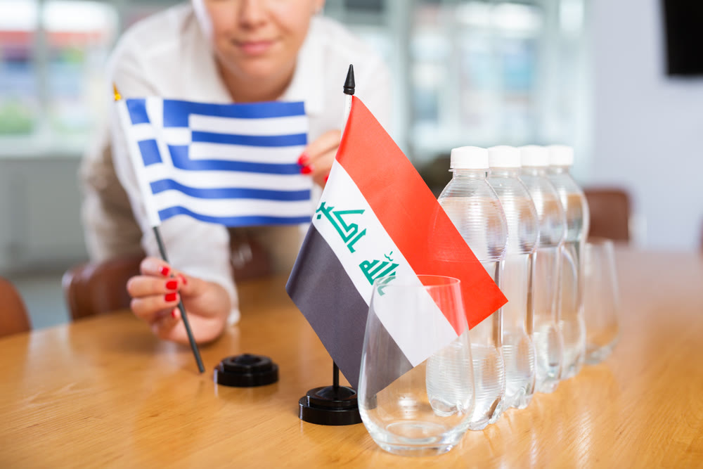 Employee of delegation prepares negotiating table - sets up flag of Greece and Iraq