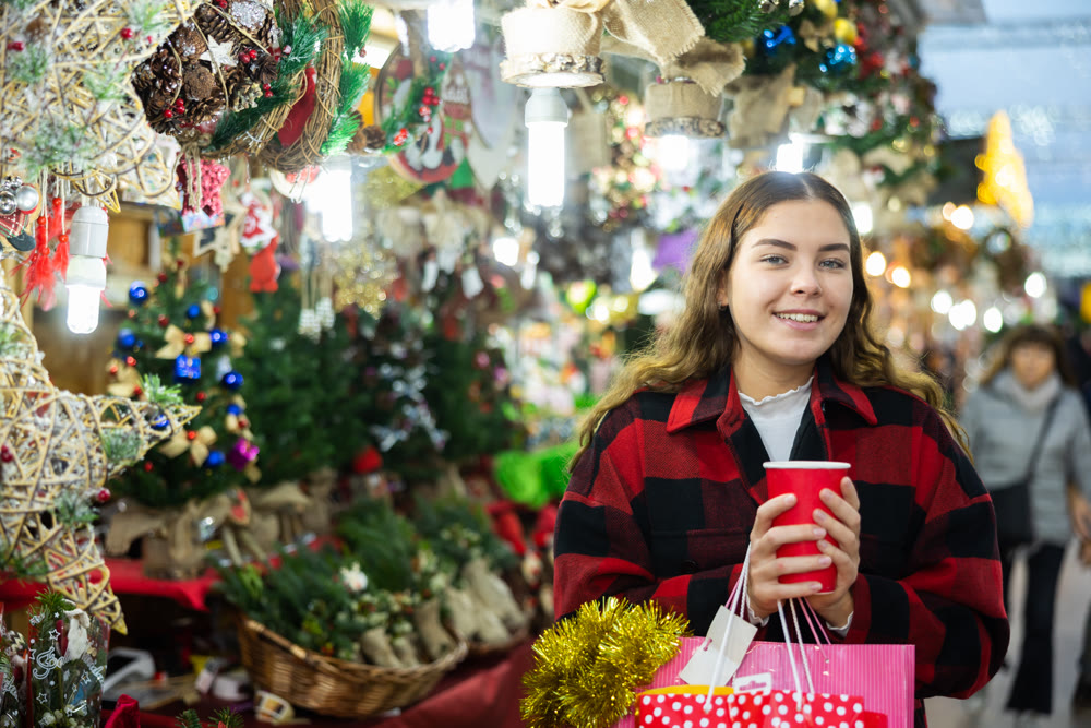 Girl with paper cup of warm drink walking at Christmas market