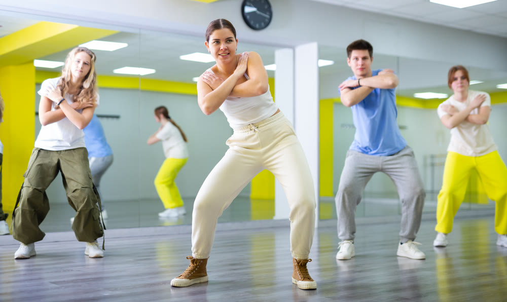 Confident sporty teenage dancers performing energetic dancing movements in modern studio with mirrors