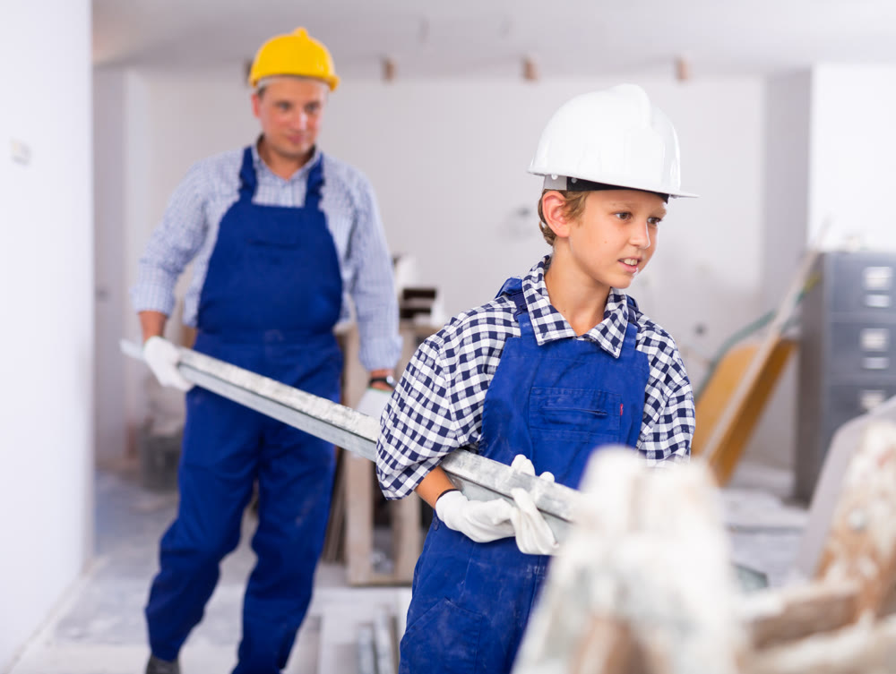 Cheerful young boy in overall carrying metal plank