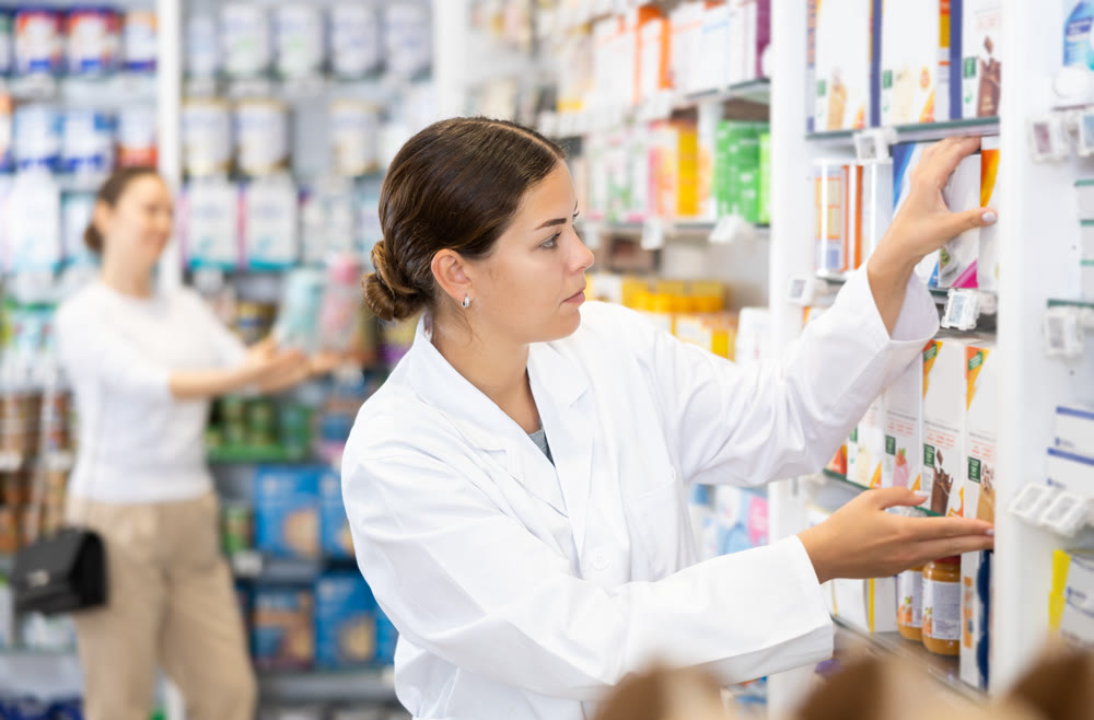In apotheke, pharmacist corrects display cases, puts in order cabinet with baby formula and porridge
