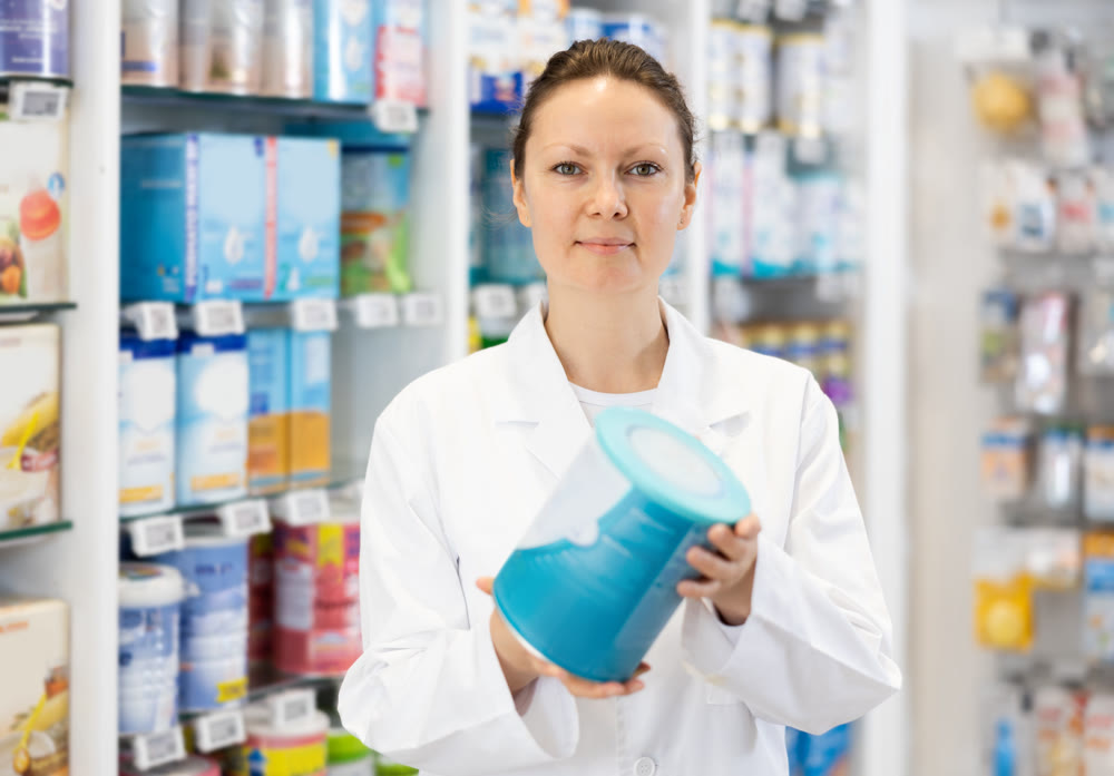 Portrait of female pharmacist in sales hall of a pharmacy, demonstrating jar of baby food