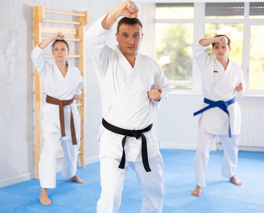 Woman and man in kimono standing in fight stance during group karate training in gym