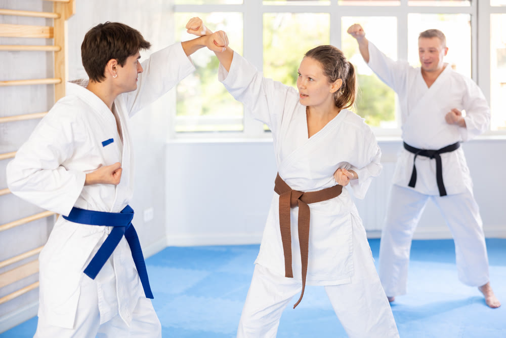 Woman and man in pairs exercising karate movements during group training in gym