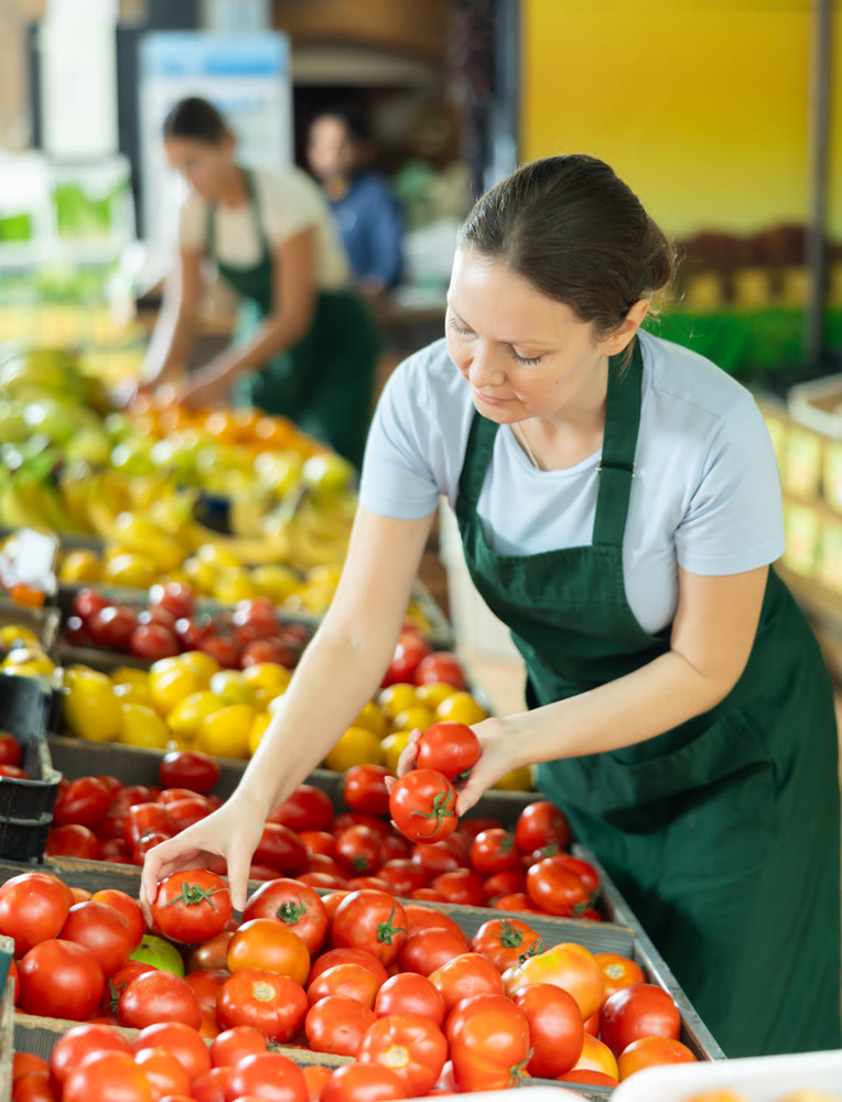Female employee was distracted for minute and stands smiling with ripe tomato in hands